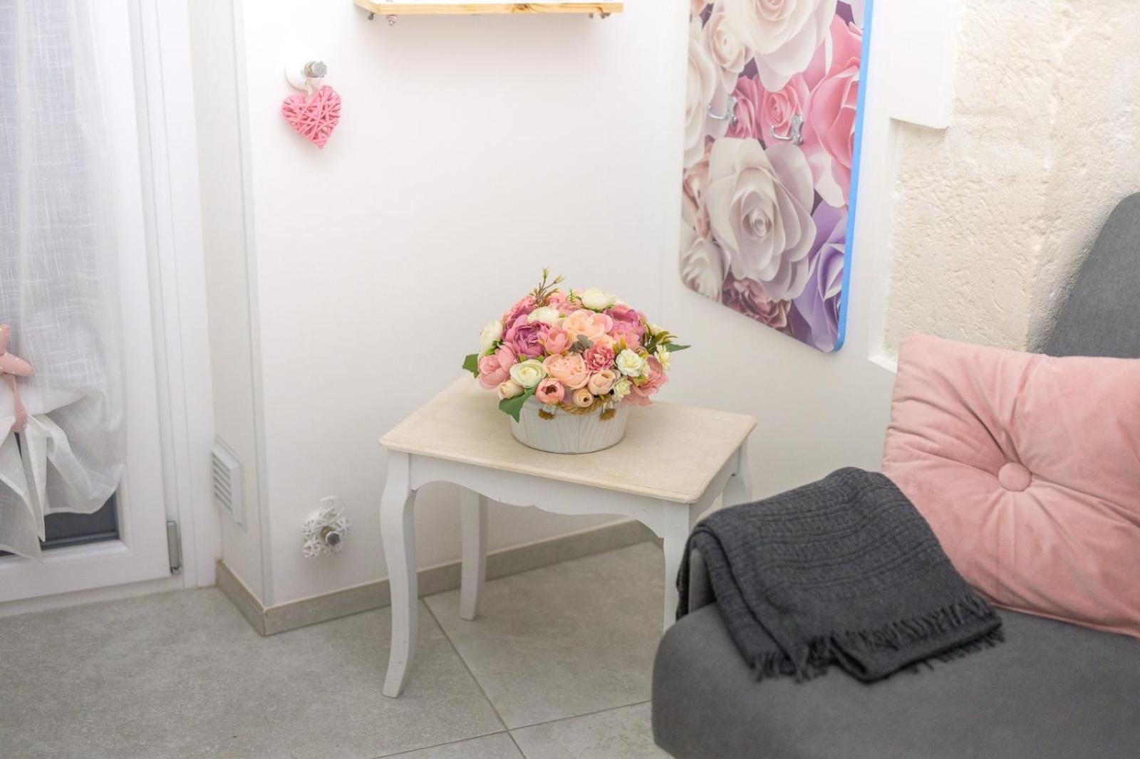Angolo con consolle, composizione di fiori, poltroncina rosa e teli preparati per gli ospiti
