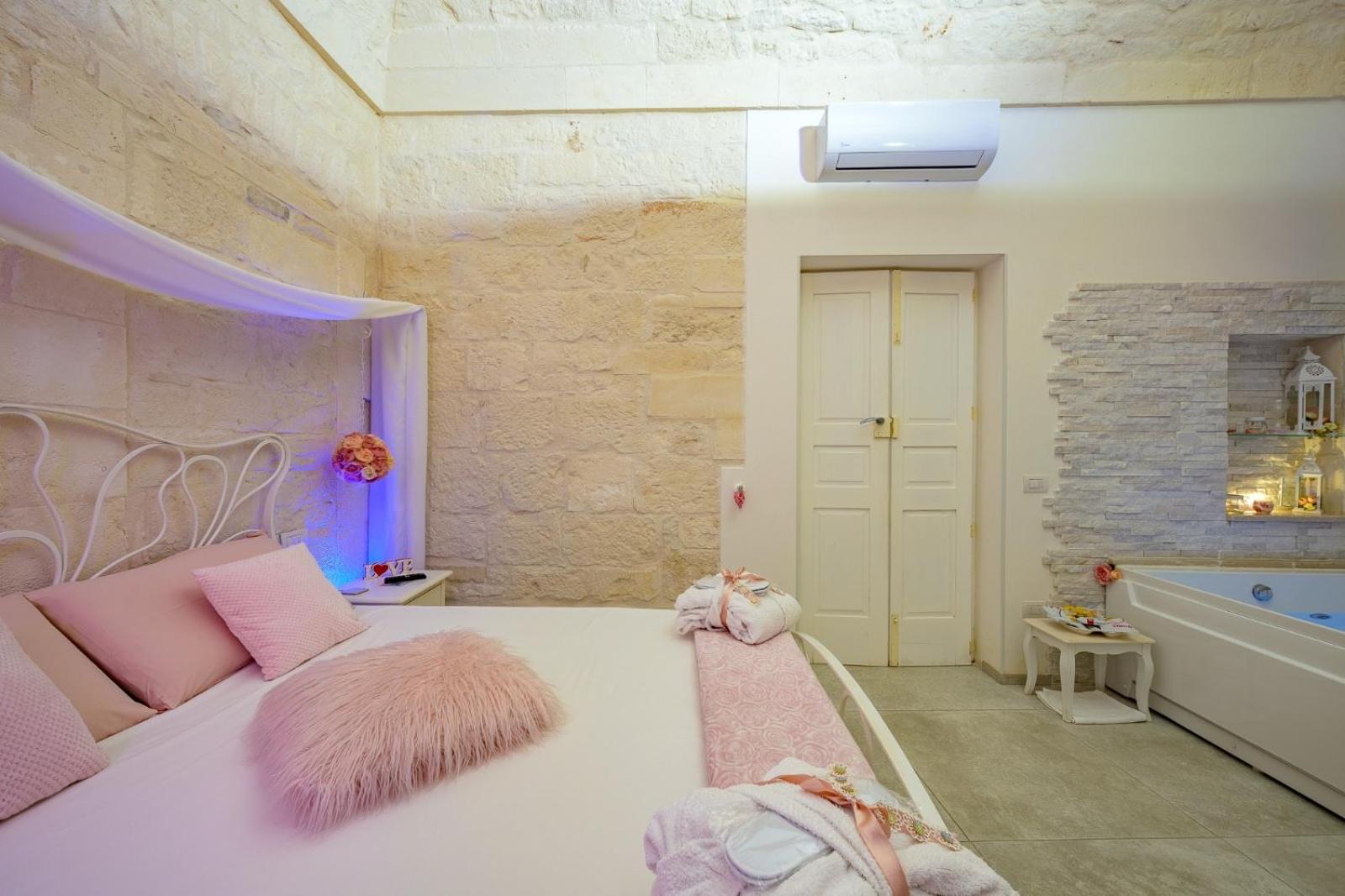 Il letto matrimoniale di Casa Deky con cuscini rosa sotto la volta in pietra, con la vasca idromassaggio a lato